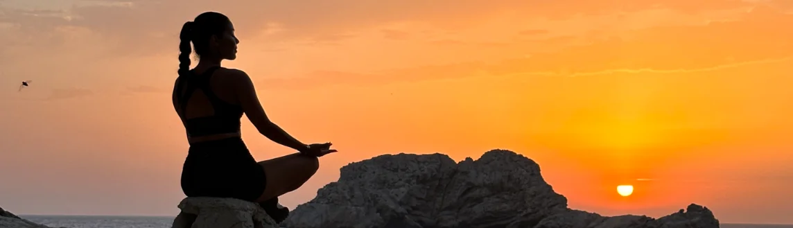 Yoga pose silhouette at sunset on an Ibiza cliff